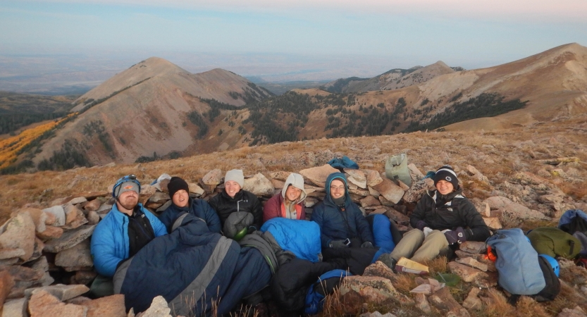 A group of people sit huddled together in a desert landscape and smile for the photo.